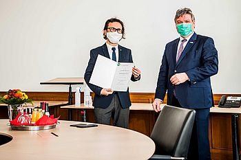 Eine Person hält ein Zertifikat in der Hand und steht neben einer anderen Person